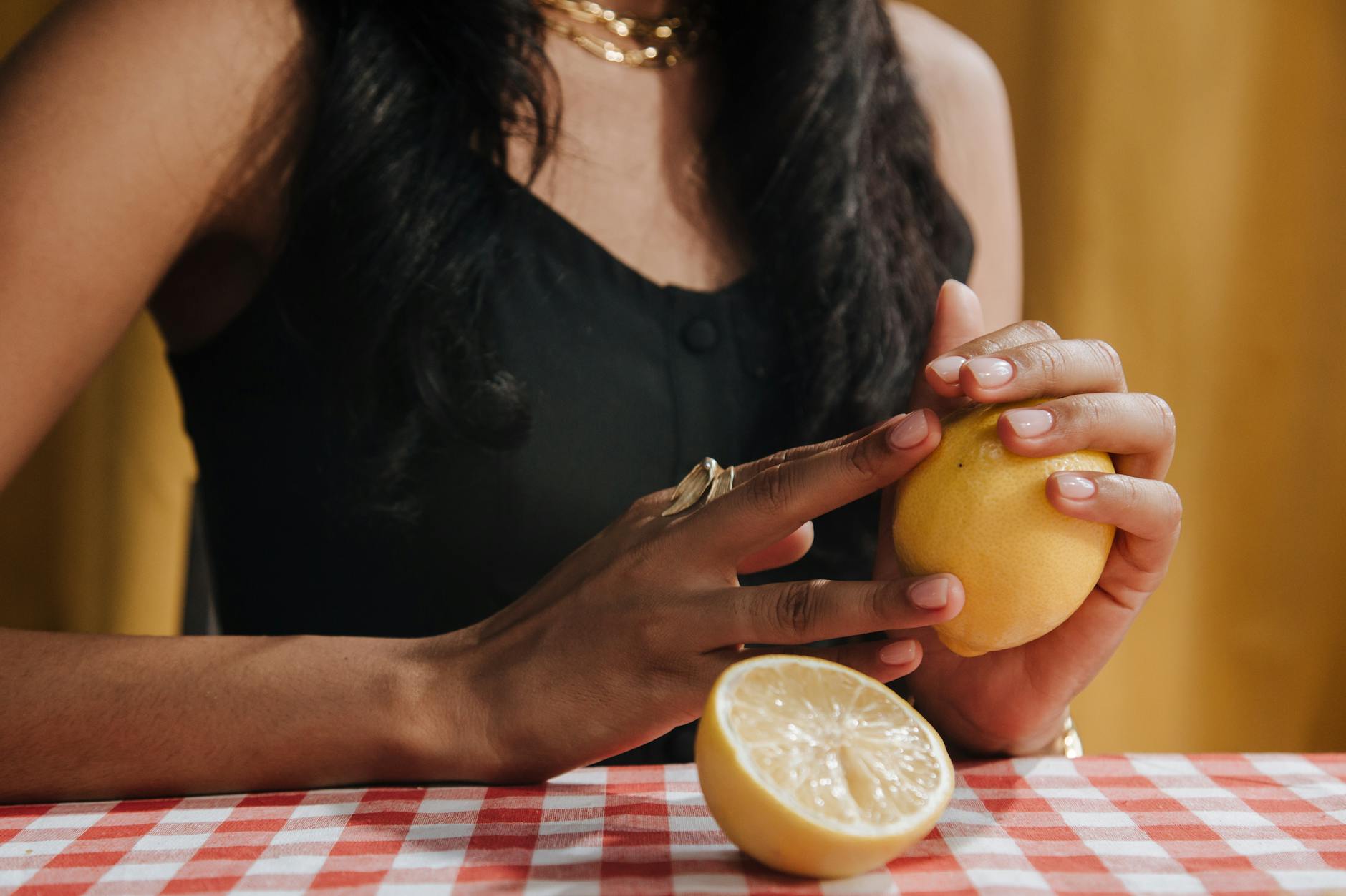 Una donna con capelli neri tiene un limone fresco al tavolo da pranzo, simbolo di freschezza e sensibilità