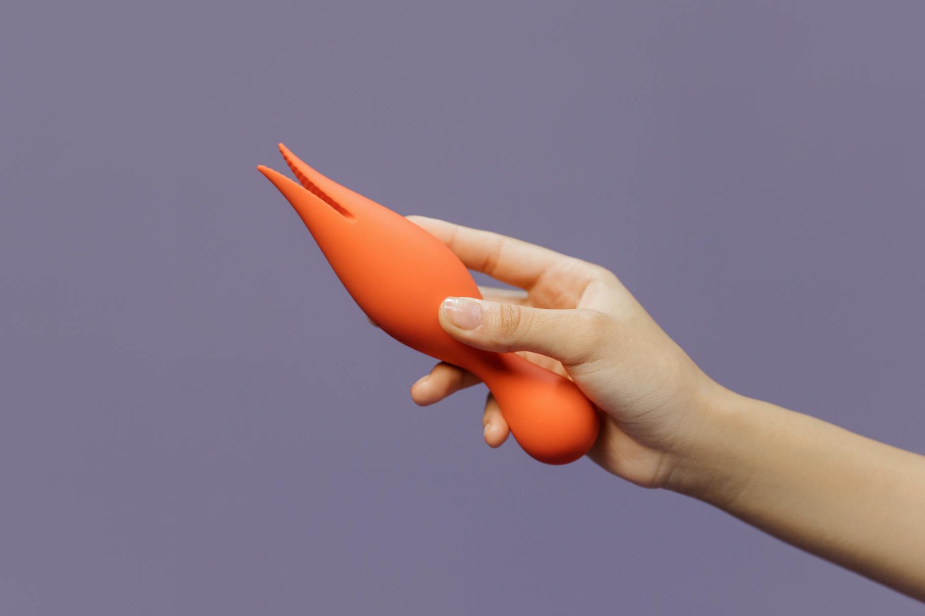 Mano che tiene un vibratore clitorideo moderno su sfondo minimalista viola