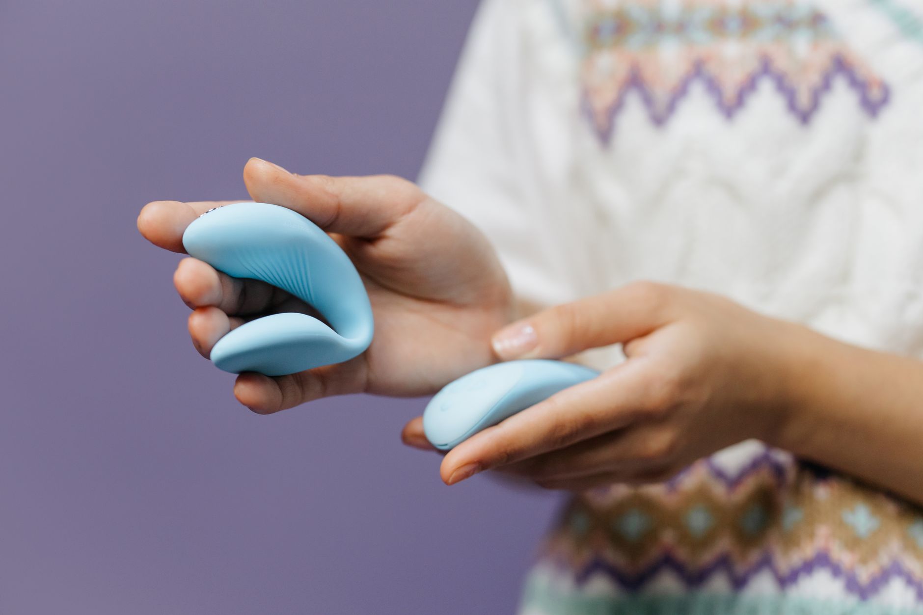 Mani che tengono delicatamente un vibratore azzurro su sfondo viola, simbolo di intimità e stimolazione consapevole.