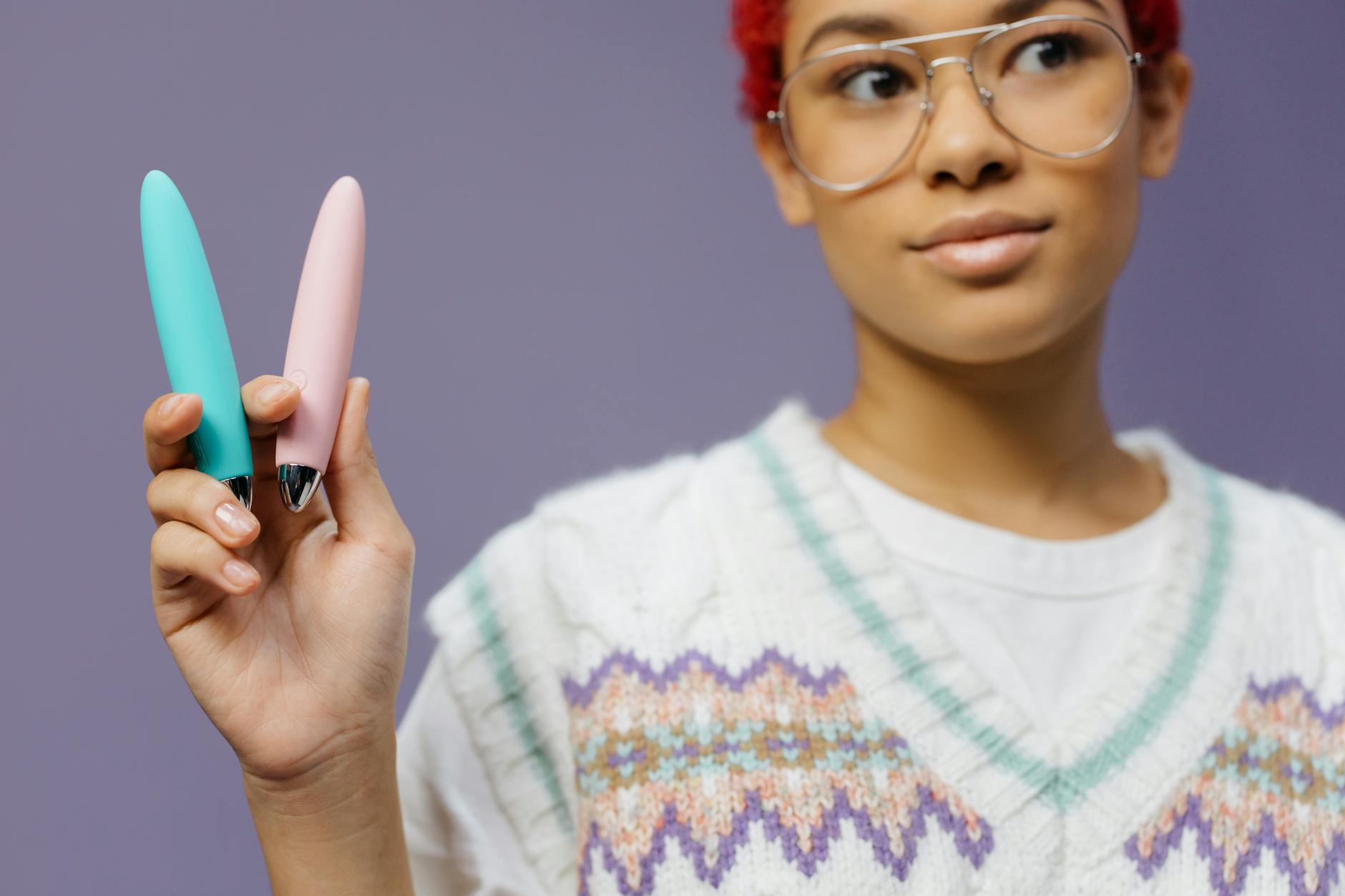 Una donna tiene due vibratori colorati contro uno sfondo viola, simboleggiando il piacere e l'esplorazione consapevole