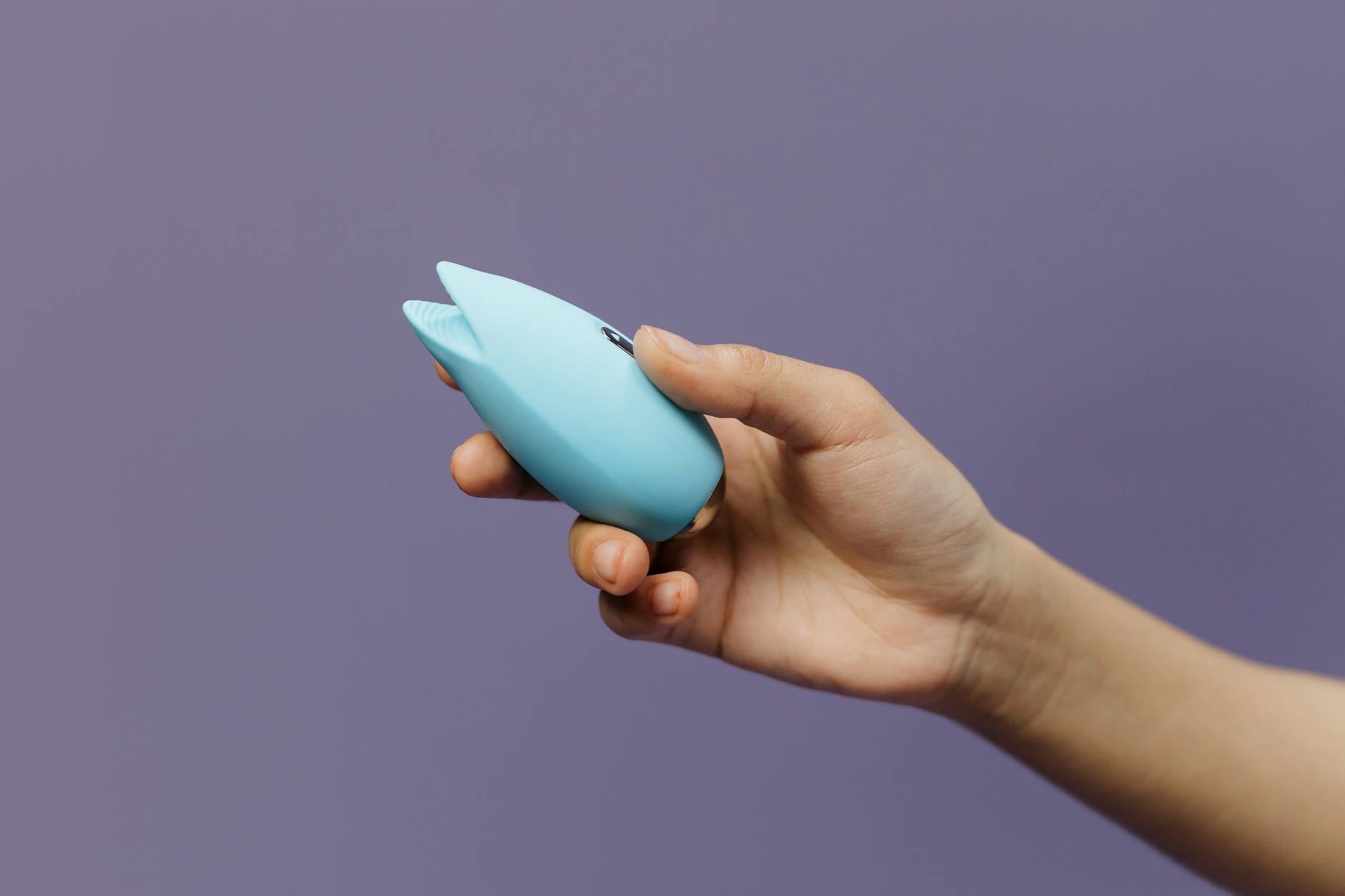 Un vibratore in silicone blu tenuto in mano su uno sfondo viola, celebrando l'auto-amore e la sessualità consapevole