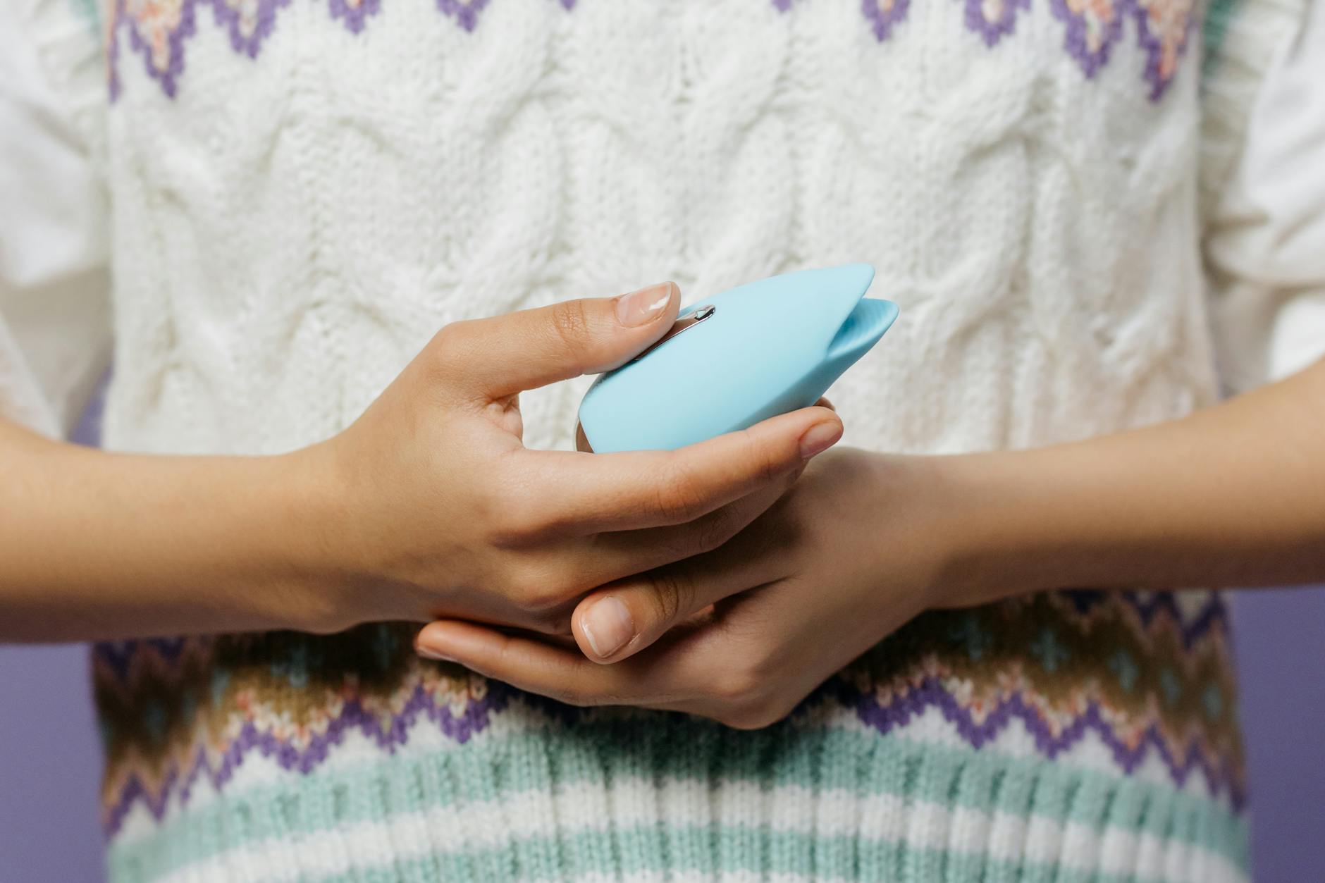 Primo piano di mani che tengono un massaggiatore personale blu contro un maglione lavorato a maglia.